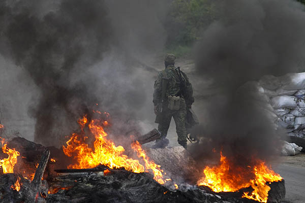 A pro-Russian separatist guards a checkpoint while walking near burning tyres near the town of Slaviansk in eastern Ukraine May 2, 2014. Ukraine launched a "large-scale operation" to retake the eastern town of Slaviansk, pro-Russian separatists there said on Friday, in an escalation of violence in what has become the worst confrontation between Russia and the West since the Cold War. REUTERS/Baz Ratner (UKRAINE - Tags: POLITICS CIVIL UNREST)